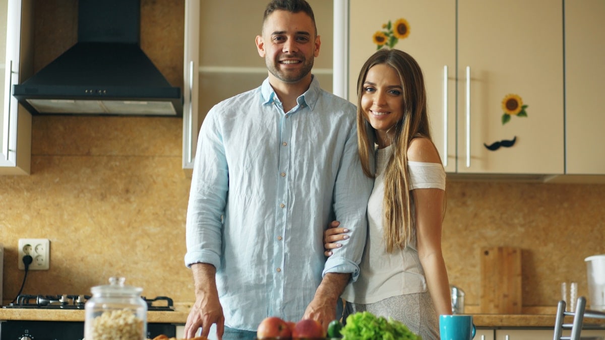 Portrait of loving couple cooking breakfast smiling ang looking into camera in the kitchen at home